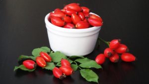 Vibrant red rose hips in a ceramic bowl atop a dark wooden table, emphasizing freshness and natural produce.